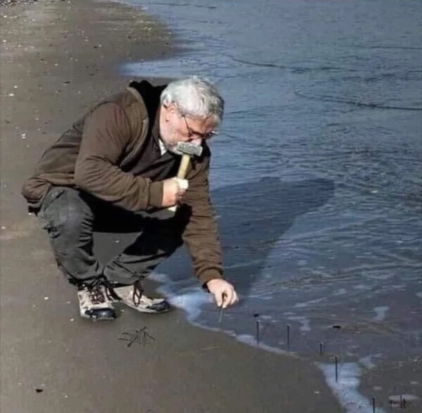 Guy Hammering Nails Into Sand meme about work